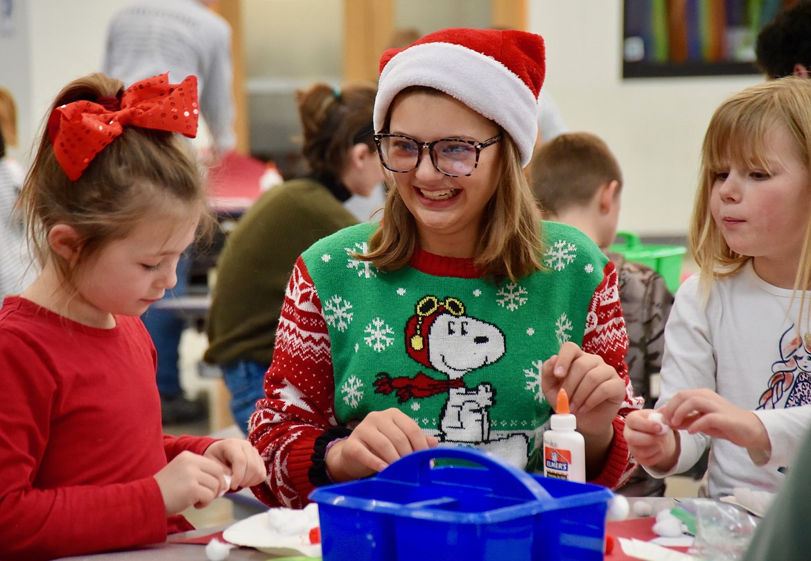 Flathead High School student Ada Milner, center, laughs while helping first-graders Harper Allison, left, and Aria Bowman at Rankin Elementary School Friday afternoon. FHS Speech and Debate team members spent time helping the younger students with making a paper Santa. (Heidi Desch/Daily Inter Lake)