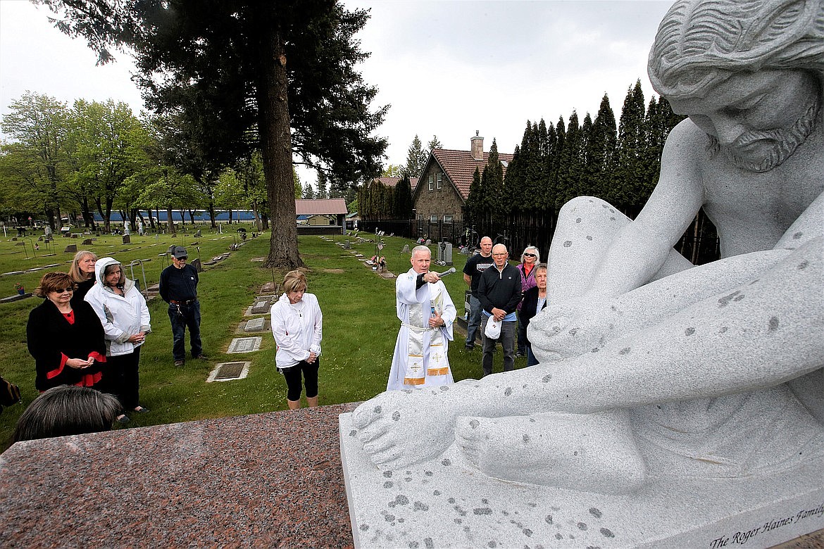 Father John Mosier blesses a statue of Jesus Christ at St. Thomas Cemetery on Monday as church members and friends look on.