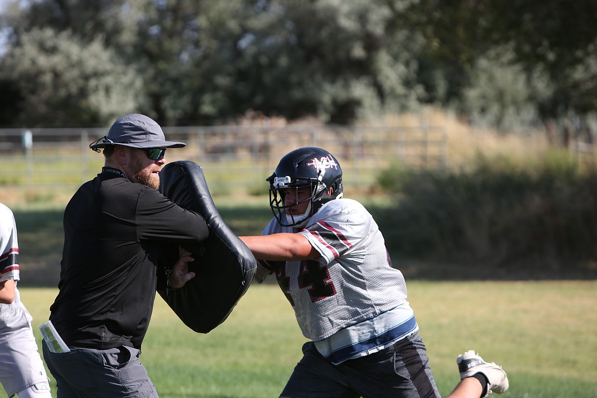 A former ACH lineman and 1990 graduate of the school, Brandon Walsh, left, teaches a Warrior lineman during practices.