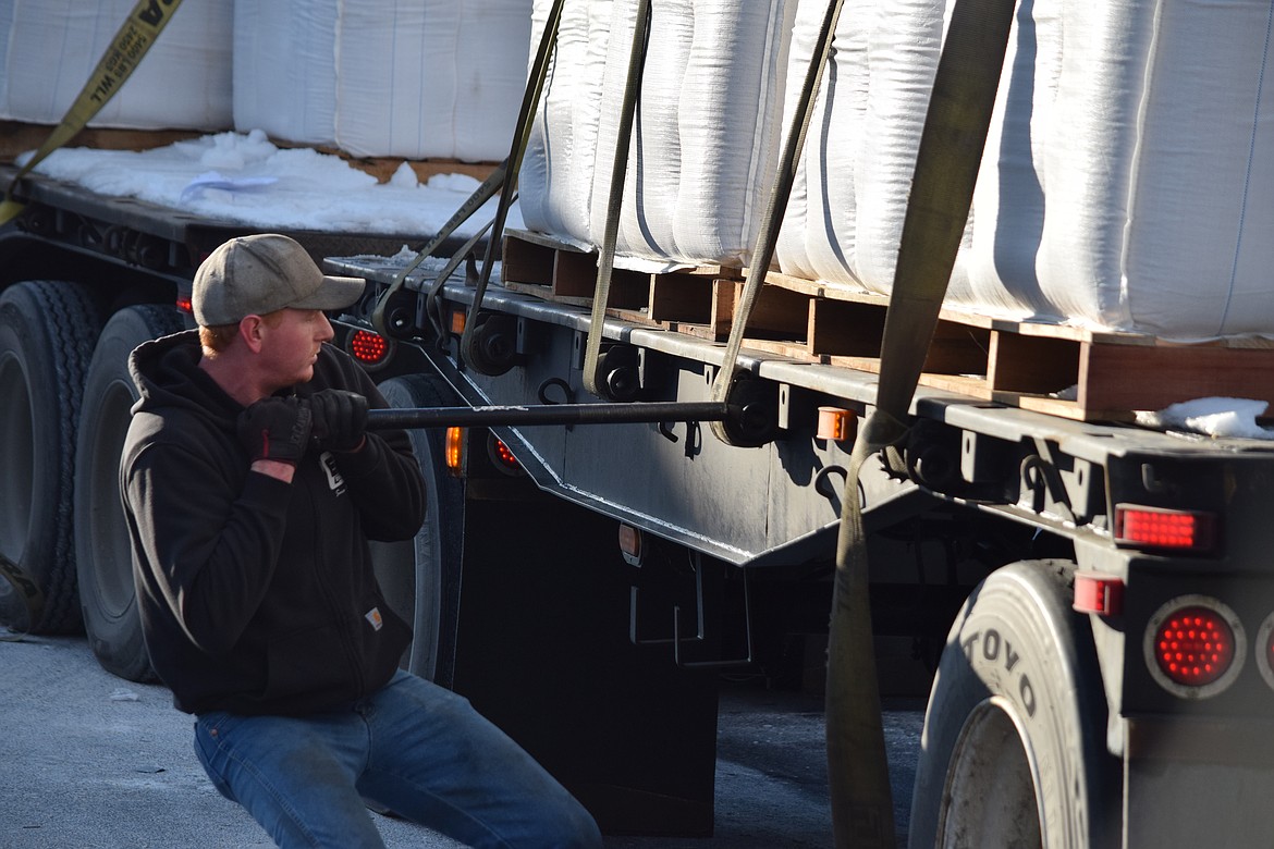 Big rig driver Theron Wood uses a crowbar to tighten the straps securing a load of palm fat to the back of his big rig