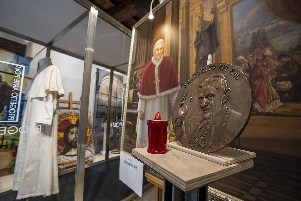 A metal disc shows Pope Emeritus Benedict XVI alongside a painting of him and one of the last cassocks worn by him before his resignation in 2013, according to the director of the Progetto Arte Poli gallery where it is displayed, near the Vatican, Tuesday, Jan. 3, 2023. The Vatican announced that Pope Benedict died on Dec. 31, 2022, aged 95, and that his funeral will be held on Thursday, Jan. 5, 2023. (AP Photo/Ben Curtis)