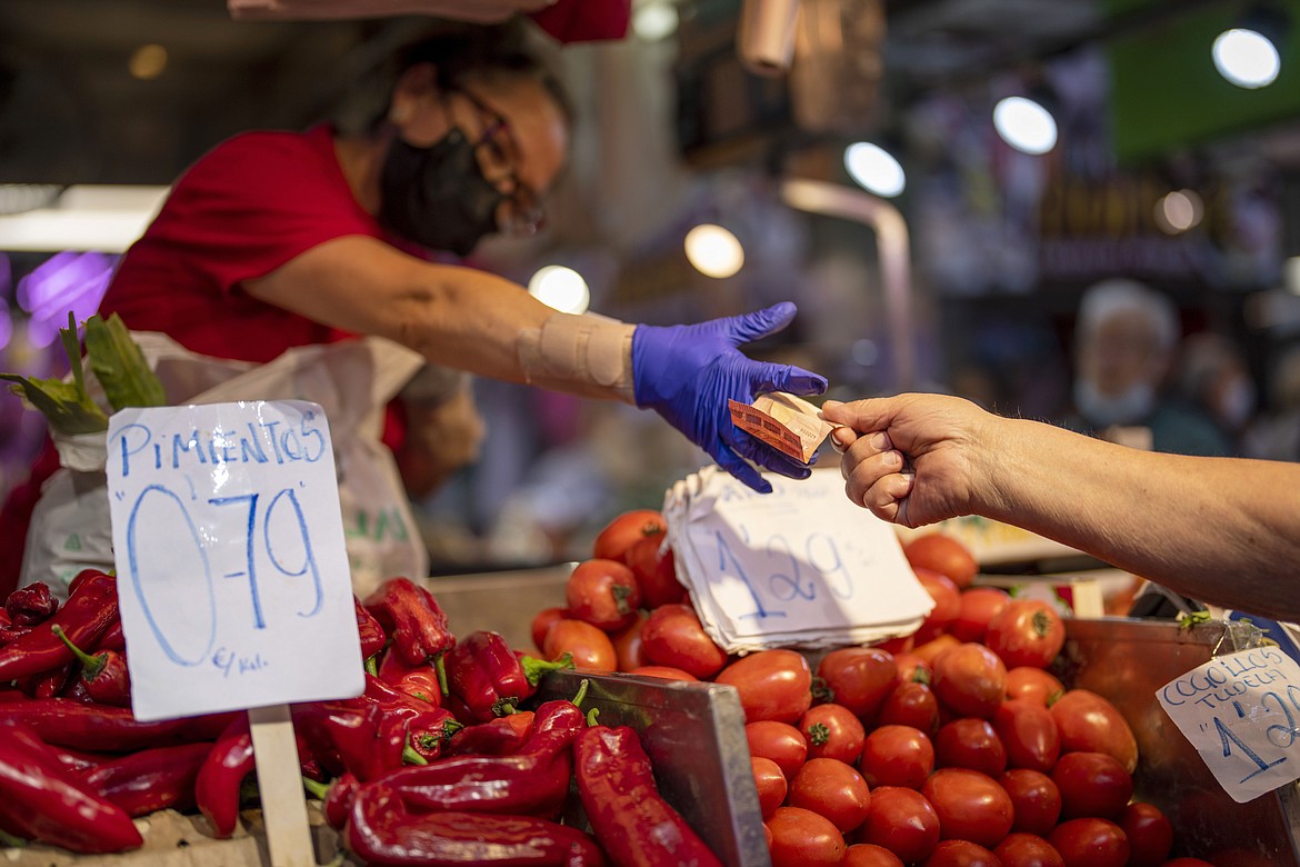 A customer pays for vegetables at the Maravillas market in Madrid, Spain, May 12, 2022. Europe ended a bad year for inflation with some relief as price gains eased again, though they still rose a painful 9.2% in December, according to data released Friday, Jan. 6, 2023. (AP Photo/Manu Fernandez, File)