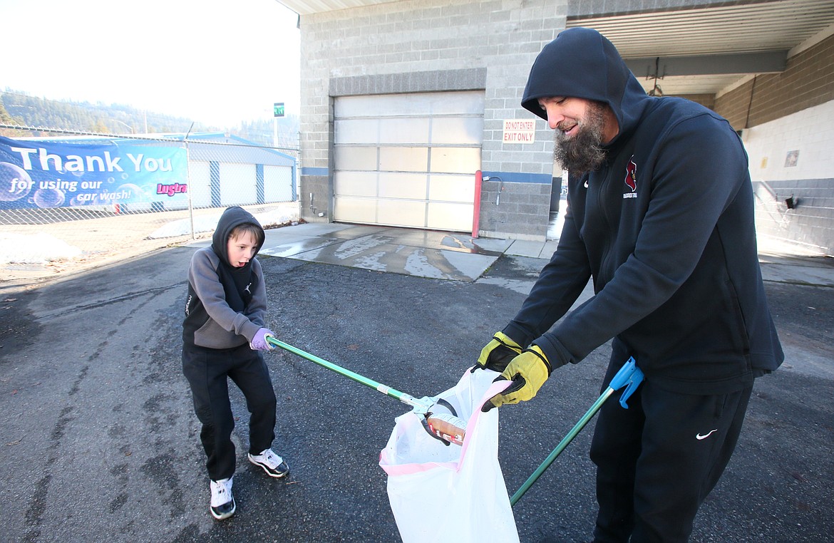 Jaxon Giles, 8, is excited to drop a discarded bottle in a trash bag held by his dad, Russ Giles, as they wander their litter pickup circuit Saturday morning in the Fernan area.