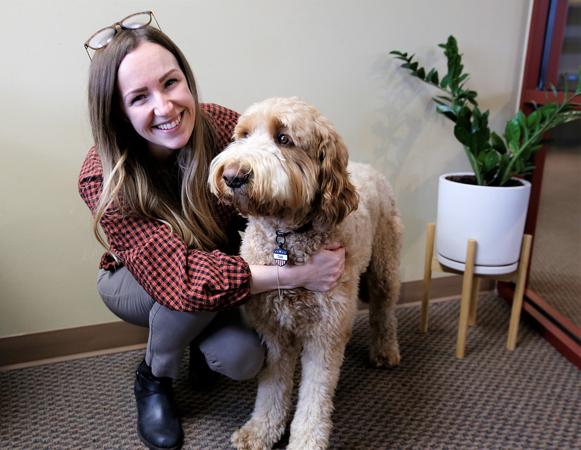 Chloe Linton, with the Coeur d'Alene Downtown Association, poses with Tuck, a Goldendoodle, at work on Thursday.