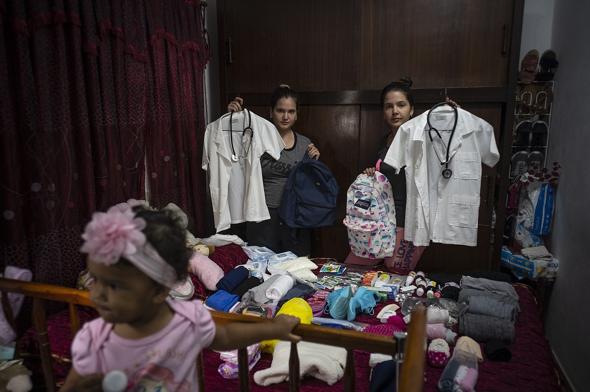 Melanie Rolo Gonzalez, right, and her sister Merlyn, pose for a photo with their medical student uniforms as they pack supplies for their journey to the U.S., in their home in Havana, Cuba, Saturday, Dec. 10, 2022. The sisters' voyage is one that hundreds of thousands of Cubans have made over the last two years in a historic wave of migration. (AP Photo/Ramon Espinosa)