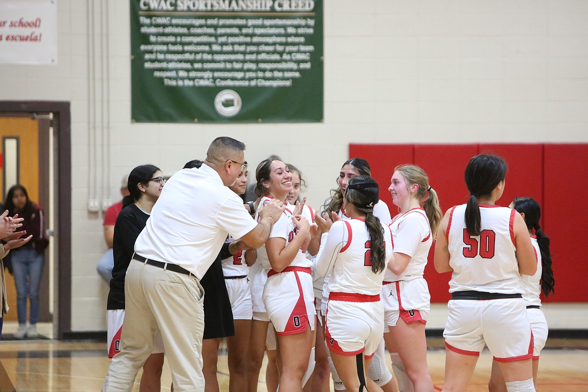 Coaches and players from Othello surround senior Briana Andrade, center, after she hit a three-pointer to give her 1,000 career points in Tuesday night’s win over East Valley (Yakima)