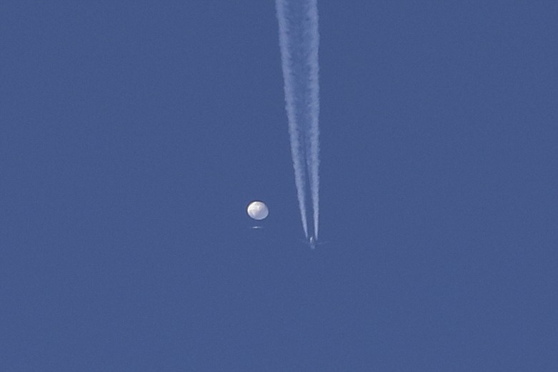 In this photo provided by Brian Branch, a large balloon drifts above the Kingstown, N.C. area, with an airplane and its contrail seen below it. The United States says it is a Chinese spy balloon moving east over America at an altitude of about 60,000 feet (18,600 meters), but China insists the balloon is just an errant civilian airship used mainly for meteorological research that went off course due to winds and has only limited “self-steering” capabilities. (Brian Branch via AP)