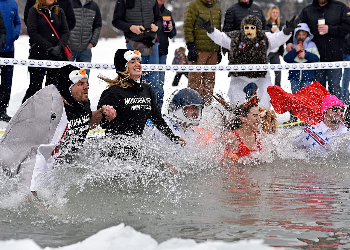 Participants dressed in costumes splash into cold water at the Penguin Plunge on Saturday at City Beach. (Whitney England/Whitefish Pilot)