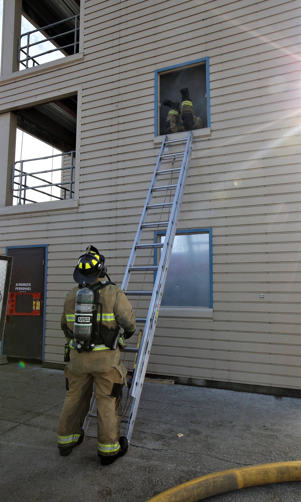 A Coeur d'Alene firefighter waits at the bottom of a ladder while another firefighter climbs through a window during training exercises Thursday.