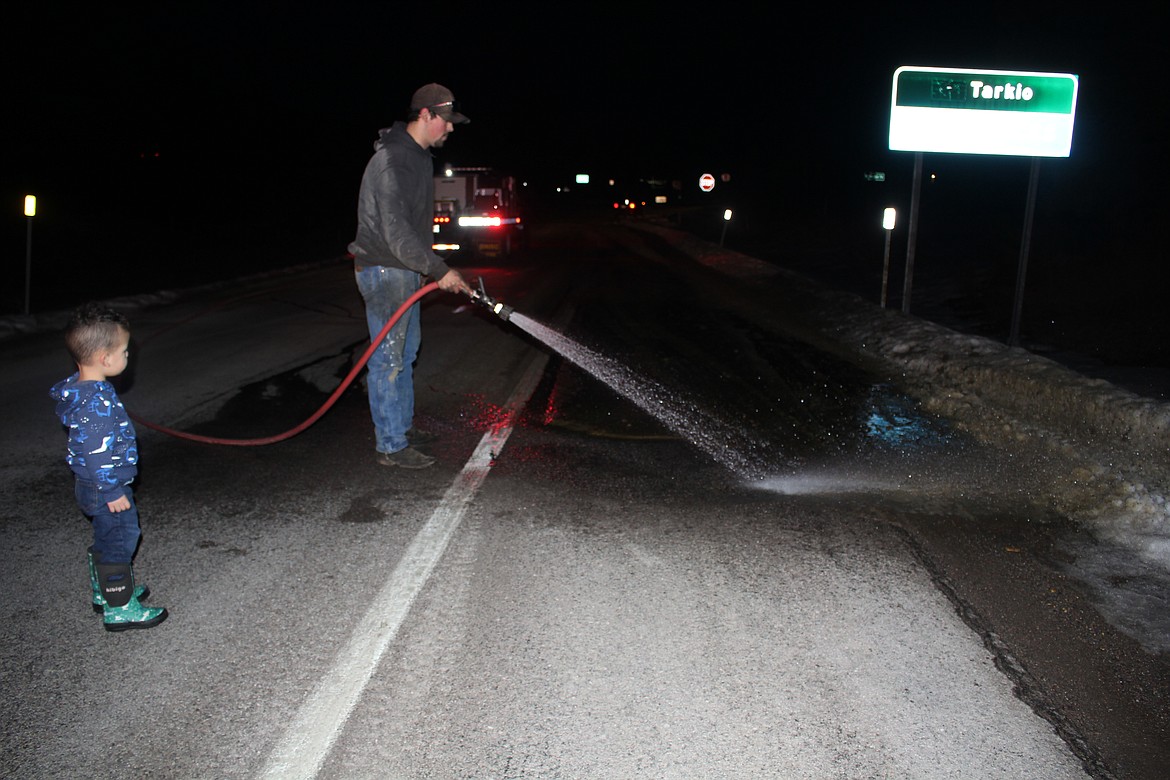 Tarkio Fire Chief Josh Pecora hoses off livestock excrement that was dumped at the I-90 Tarkio exit. His son, Mason, supervises from a safe distance. (Monte Turner/Mineral Independent)