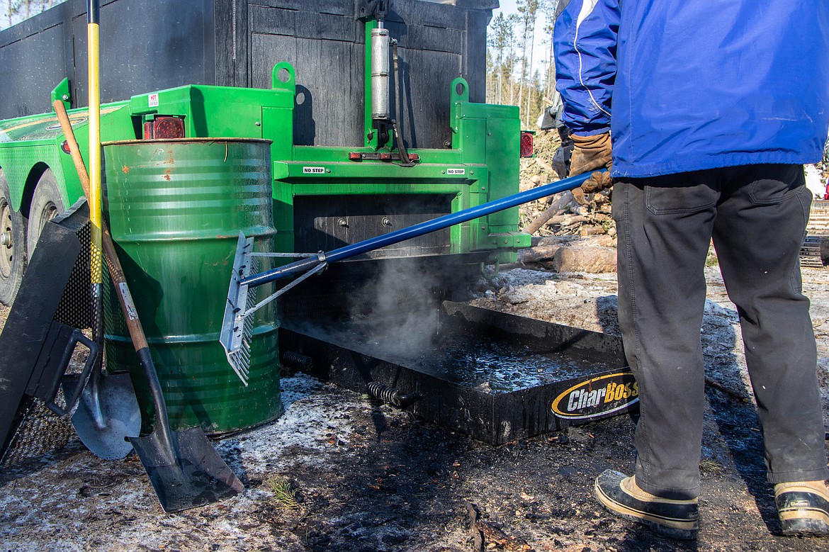The CharBoss, a machine that converts woody material into biochar, is seen on Feb. 16, 2023 at a showcase event near Coram. The charred material exists the machine into water, where it is raked out. (Kate Heston/Daily Inter Lake)