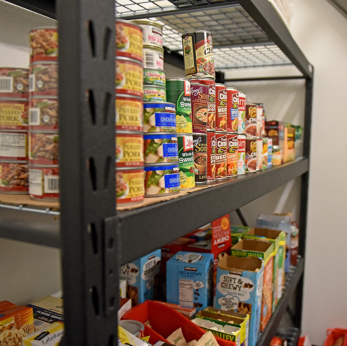 A shelf at the PAWS Pantry lined with canned goods and snacks. (Whitney England/Whitefish Pilot)