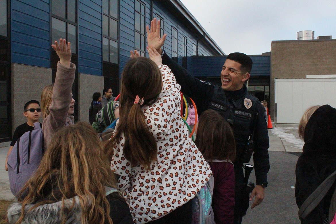 Moses Lake Police Department Officer Roland Alejo exchanges high fives with Groff Elementary students at recess after breakfast.