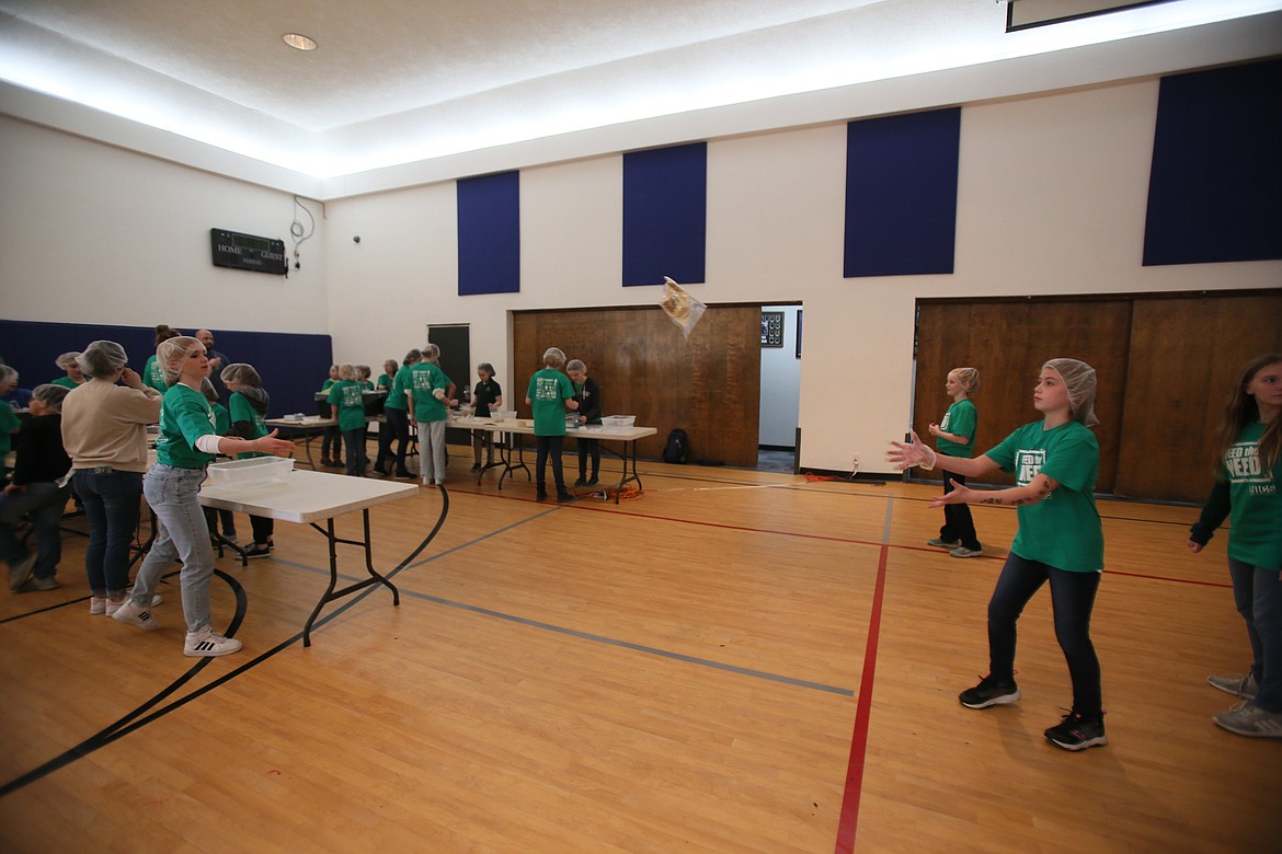 Fourth grader Ruby Mills, right, catches meals tossed by eighth grader Cheyenne Collins as they participate in the Feed the Need packing party Thursday morning in the North Idaho Christian School gym.