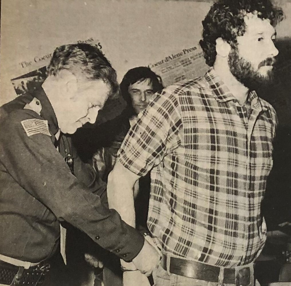 Officer Phil Collins handcuffs Press staffer David Bond while Sheriff Rocky Watson watches.