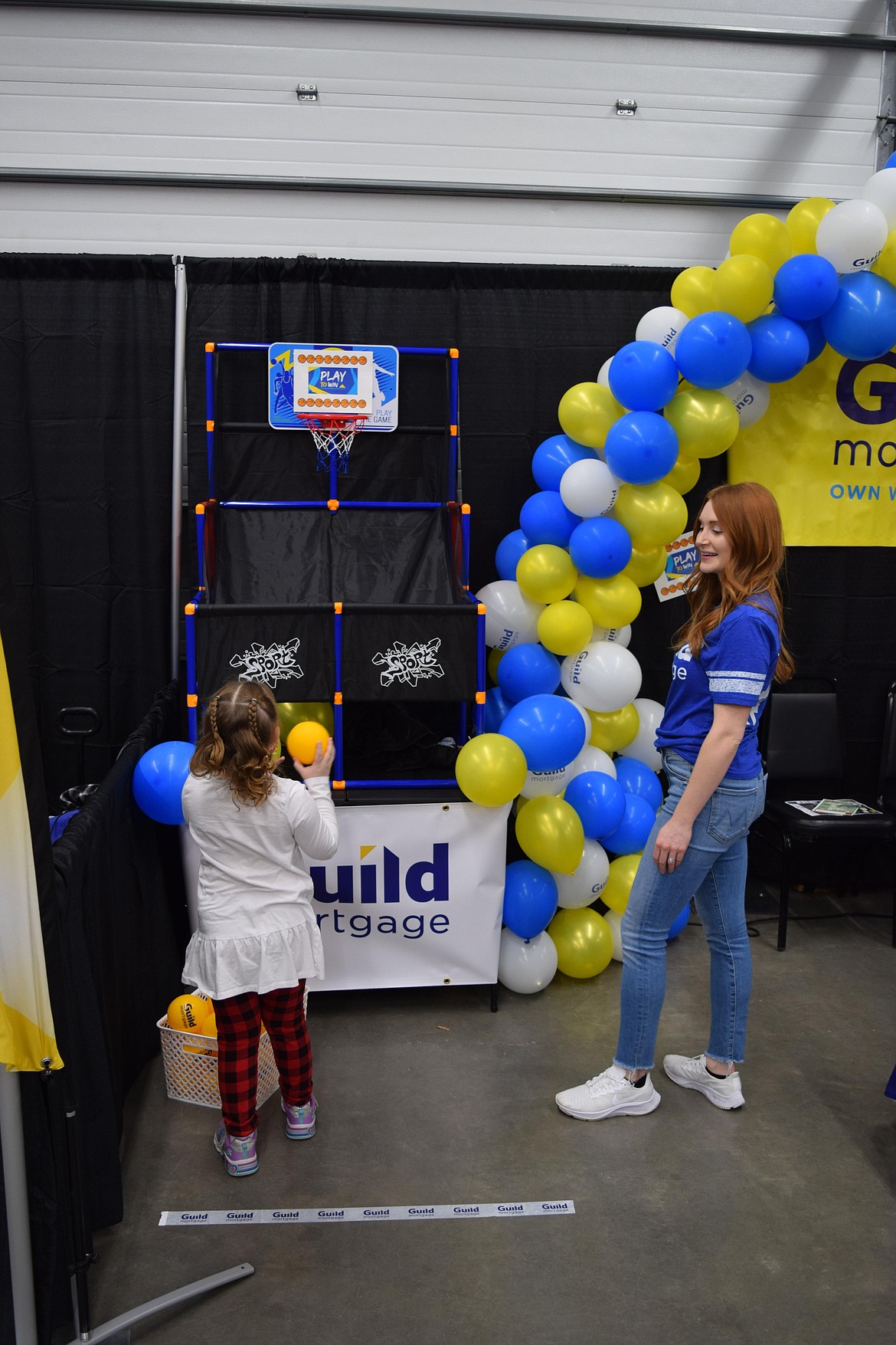 Luna Larson, 5, prepares to throw a small ball through a hoop at the Guild Mortgage booth while Guild Mortgage loan officer Callie Caniere looks on during the Moses Lake Chamber of Commerce’s annual Business Expo on Tuesday. “It’s one of our favorite events,” Caniere said.