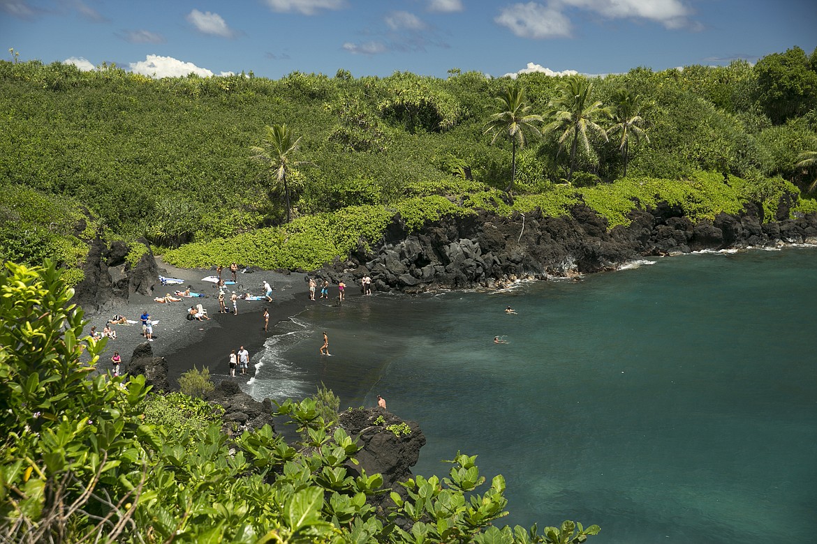 People spend time on the black sand beach at Waianapanapa State Park in Hana, Hawaii, on Sept. 24, 2014. Taking care of Hawaii's unique natural environment costs money and now the state wants tourists to help pay for it, especially because growing numbers are traveling to the islands to enjoy the beauty of its outdoors — including some lured by dramatic vistas they've seen on social media. (AP Photo/Marco Garcia, File)