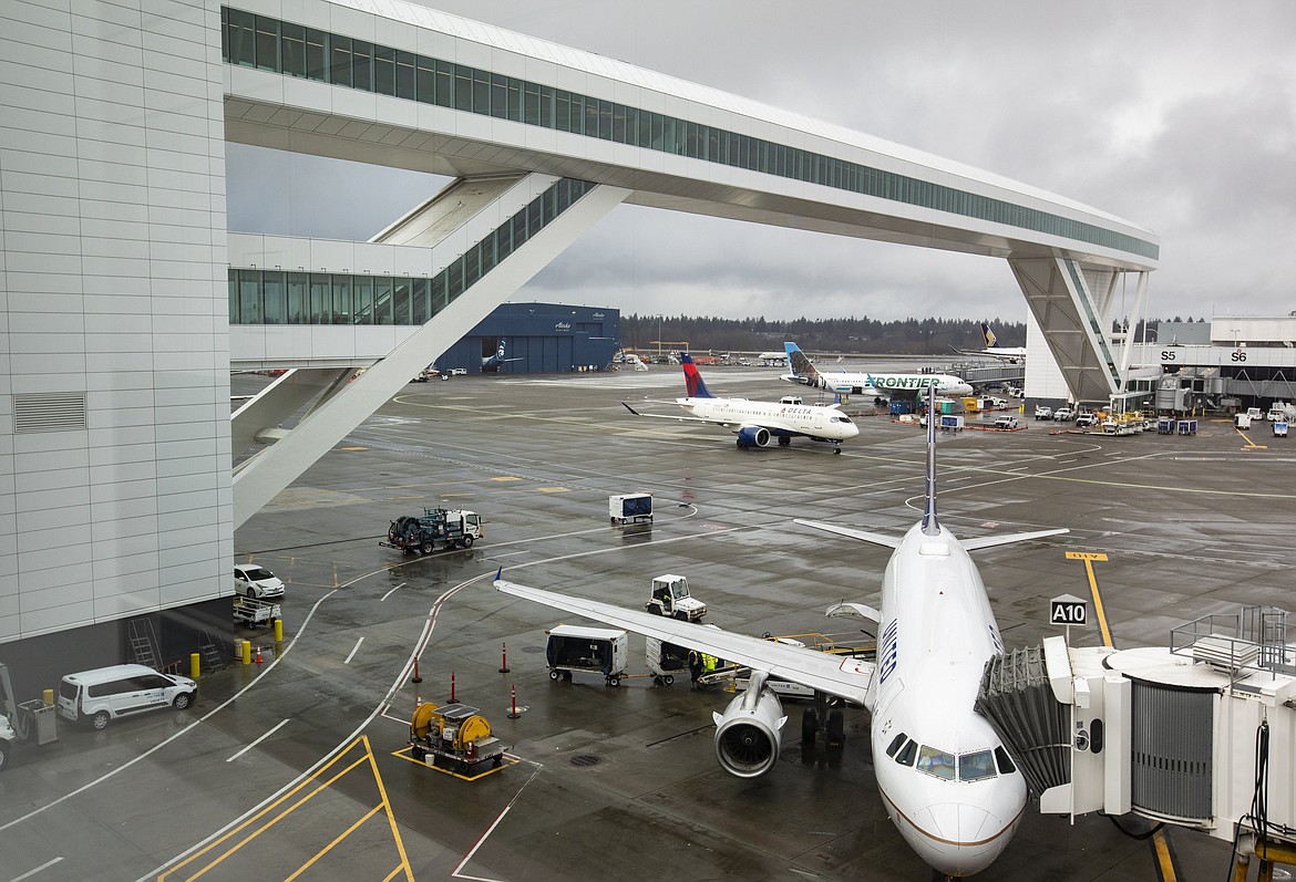 FILE - A Delta Air Lines flight, rear center, taxis under the 780-foot-long, 85-foot-high aerial passenger walkway, part of the new International Arrivals Facility at Sea-Tac International Airport, on March 3, 2022, in Seattle. The new, billion-dollar international terminal at Seattle's airport opened last year and was supposed to fit 20 large planes side by side. But The Seattle Times reports it can only accommodate 16 planes simultaneously because of design flaws. The Port of Seattle, which operates the airport, and Clark Construction, which built the new facility, have both filed lawsuits over the capacity issue. The Port and Clark Construction declined to comment on the pending litigation. (Ken Lambert/The Seattle Times via AP, File)