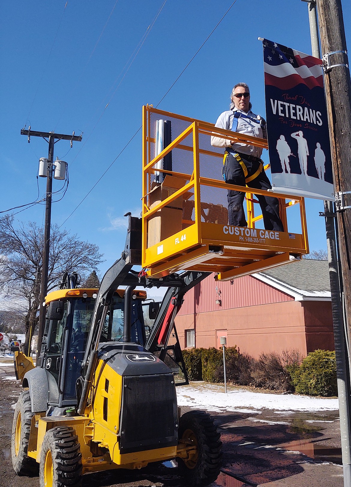 Rodney Goins, Superior Public Works Superintendent, hangs one of the banners dedicated to veterans in the new lift basket. (Monte Turner/Mineral Independent)