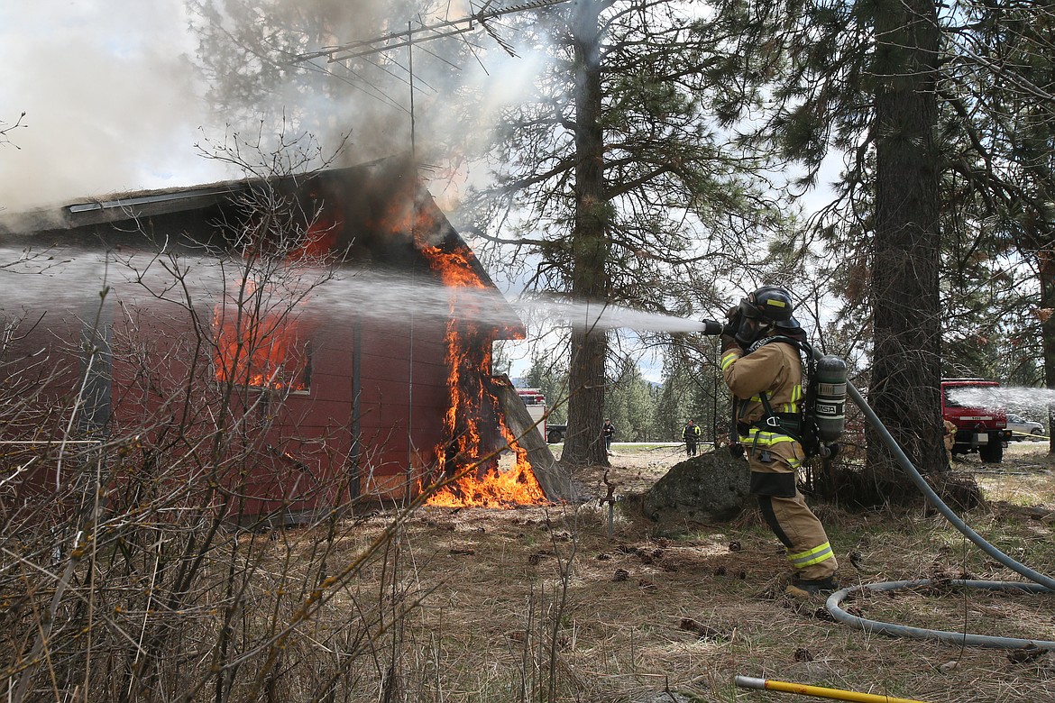 Hauser Lake Fire Protection District firefighter Kyle Andrews sprays the perimeter Saturday during a controlled house burning exercise.