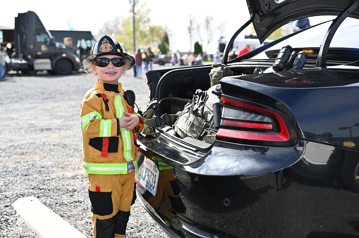 A child dressed up as a firefighter stands next to the back of a Washington State Patrol Car during the Touch a Truck fundraiser organized on Saturday by Mothers of Preschoolers.