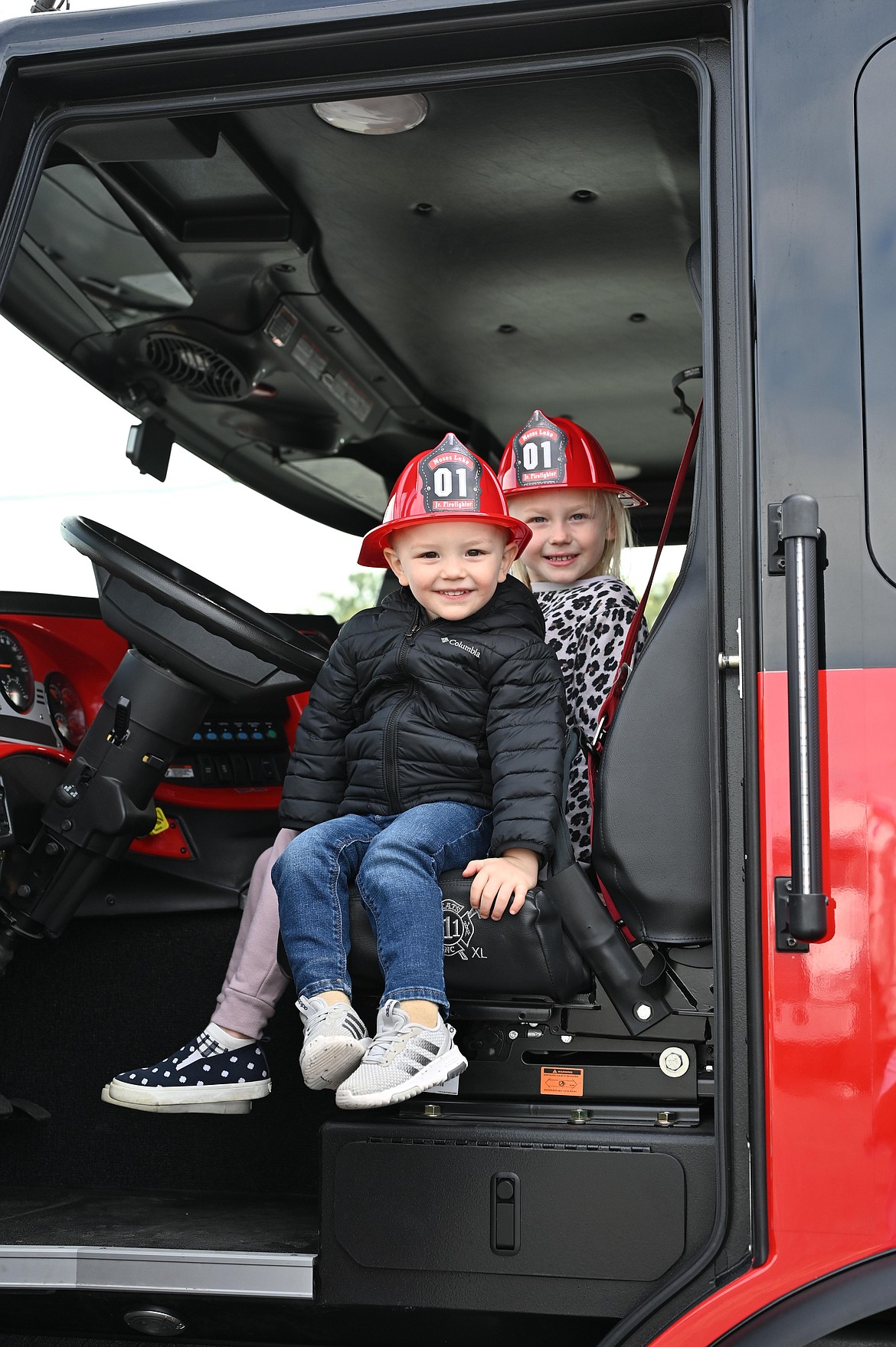 A pair of children smiles from the cab of a very big fire truck at the Mothers of Preschoolers Touch a Truck fundraiser on Saturday.