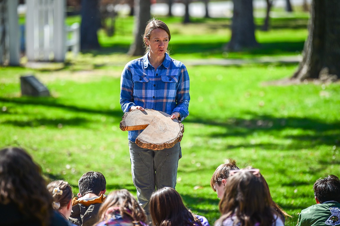 Ali Ulwelling, with the Montana DNRC, shows third-grade students from Edgerton Elementary School teacher Lexi Gilbert's class a tree ring at the DNRC forestry station at the Arbor Day celebration in Woodland Park in Kalispell on Friday, April 28. (Casey Kreider/Daily Inter Lake)