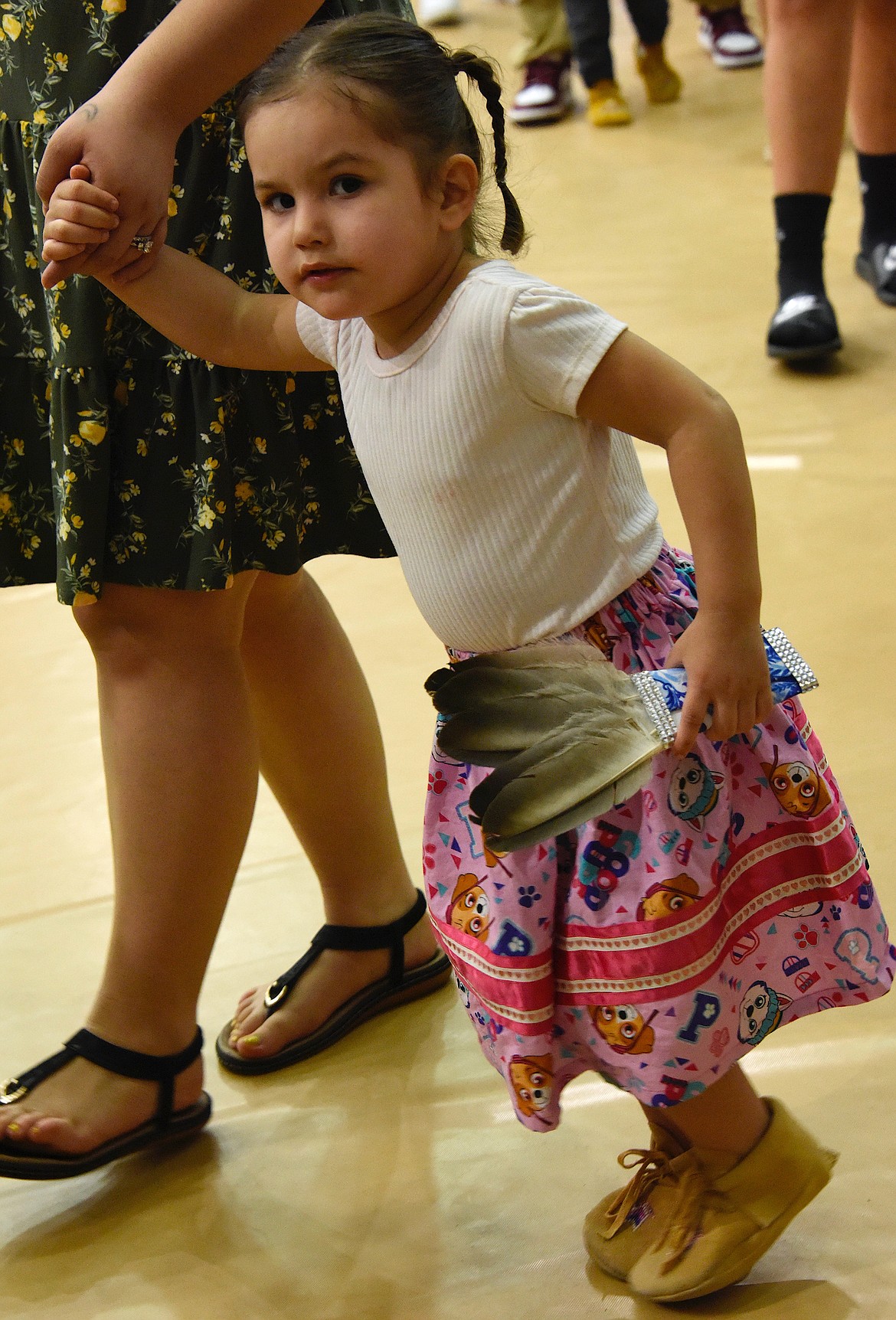 A tiny dancer with a tiny fan walks with her mom at the Head Start Pow-Wow.