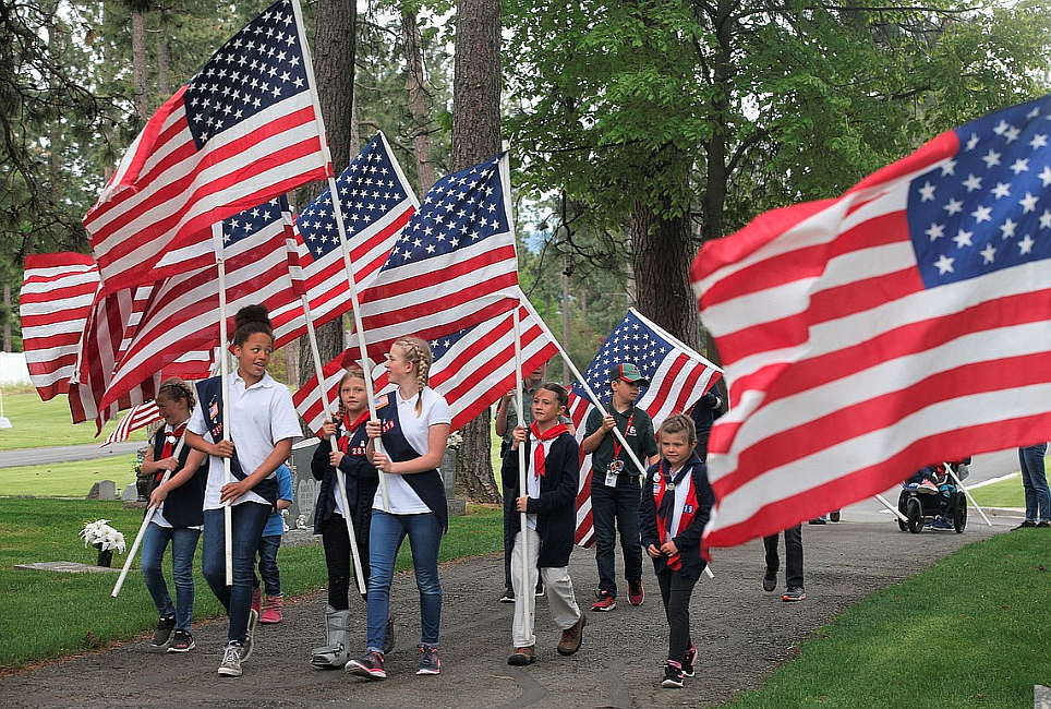 Members of American Heritage Girls and Trail Life USA boys with Real Life Ministries in Post Falls on Memorial Day 2022 carry flags in Evergreen Cemetery.