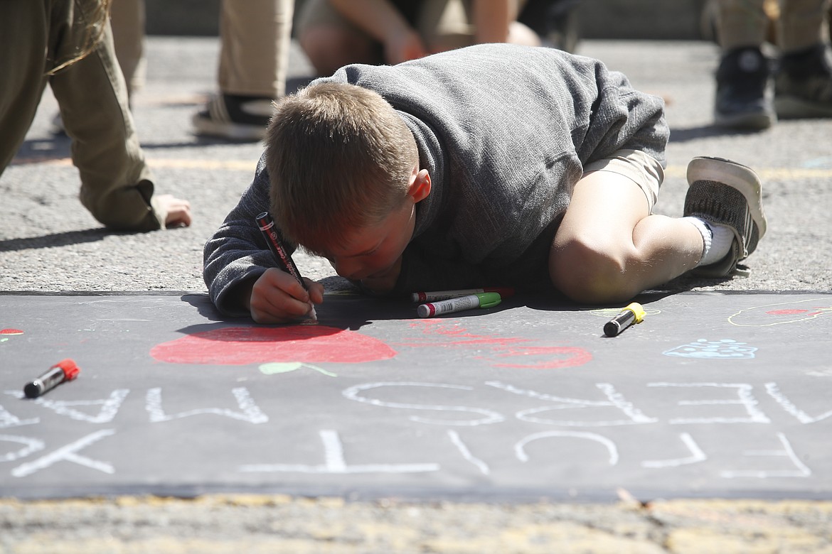 Thor Ross, Sorensen Magnet School of the Arts and Humanities third grader, focuses on a drawing for the 5th Street Farmers Market on Tuesday in downtown Coeur d'Alene.