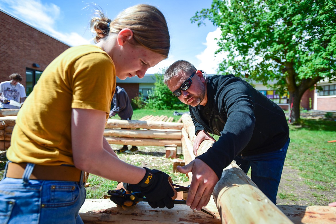 Kalispell Middle School teacher Kris Schreiner helps Paulina Holland use a scribe to draw an area on a log where a saddle notch will be cut as Schreiner's eighth-grade history students construct a log cabin on Tuesday, May 9. (Casey Kreider/Daily Inter Lake)