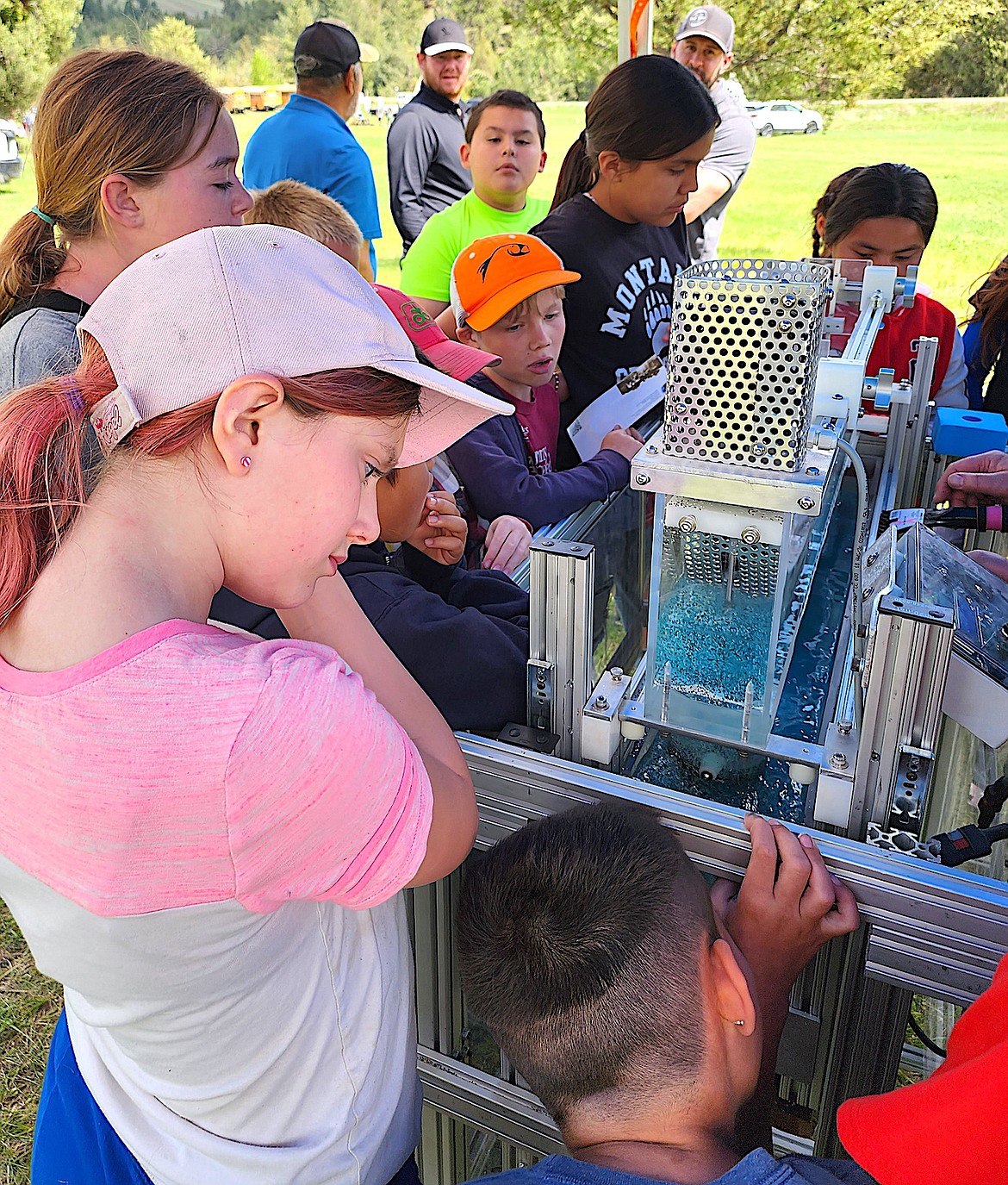 Fourth graders from St. Ignatius crowd around a model of a stream to see how different events, such as melting in the mountains, affects the water flow. (Berl Tiskus/Leader)