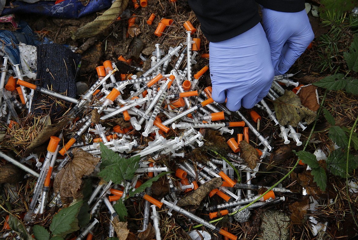 A volunteer cleans up needles used for drug injection that were found at a homeless encampment in Everett in 2017. (AP Photo/Ted S. Warren, File)