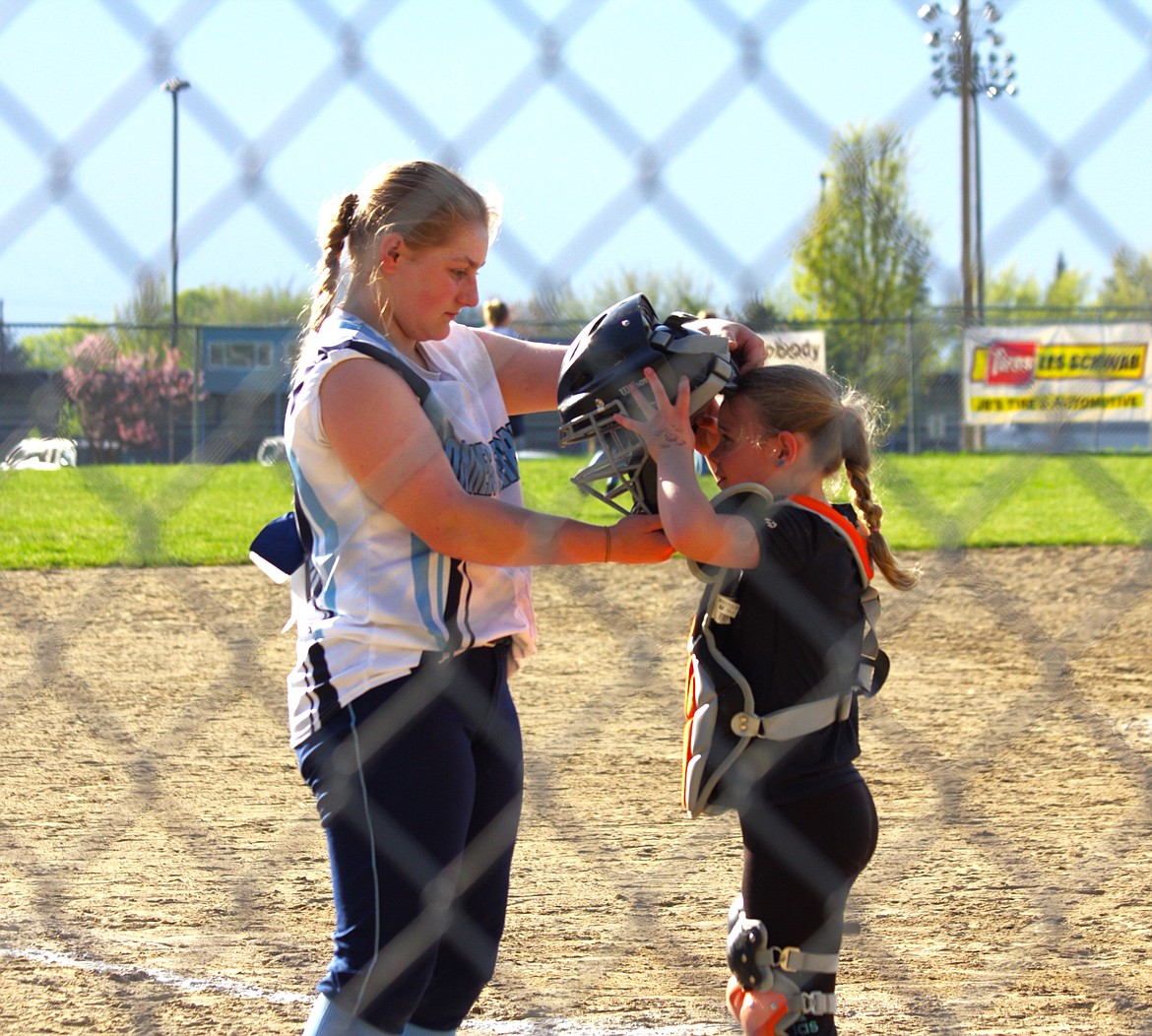 (left) Savannah Rickter, catcher for Badger softball, helps little league player with catchers gear.