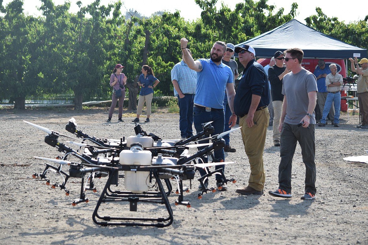 Charlie Lautenbacher (in light blue shirt), a drone pilot for Altitude Agri Services, talks with company owner Kurt Beckley as they stand over two of the company’s DJI Drones’ T-30 sprayer drones during Washington State University’s Spring Drone Day at Hayden Farms north of Pasco.