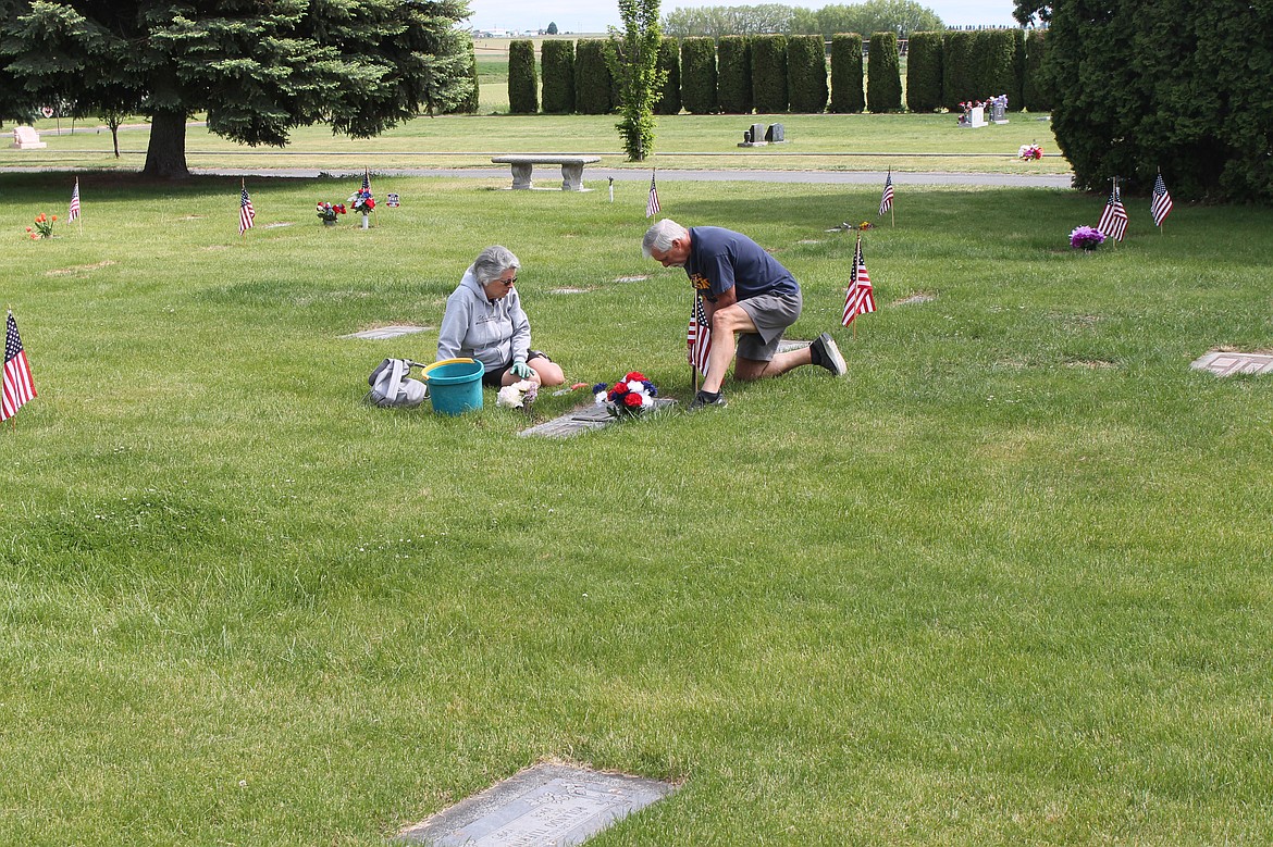 A couple decorates a grave at a local cemetery. Special services to remember military veterans are scheduled for Monday.
