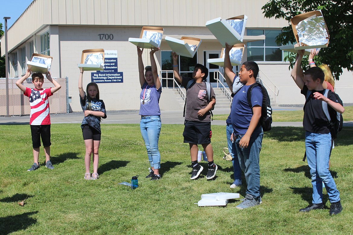 Fifth-graders hold their pizza boxes high in an attempt to focus the rays of the sun. The DIY parabolas were part of the Solar Car STEM days at Big Bend Community College.