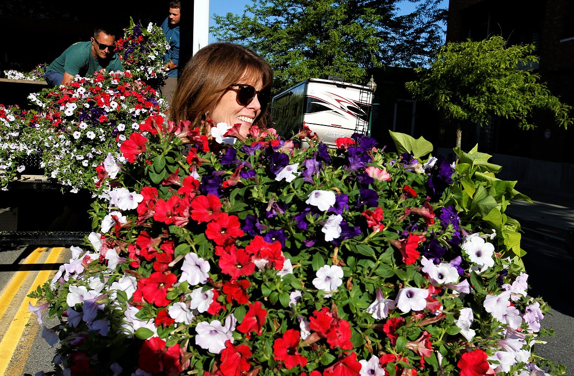 Bridget Lee carries a flower basket so it can be put in its place on Sherman Avenue on Thursday morning.
