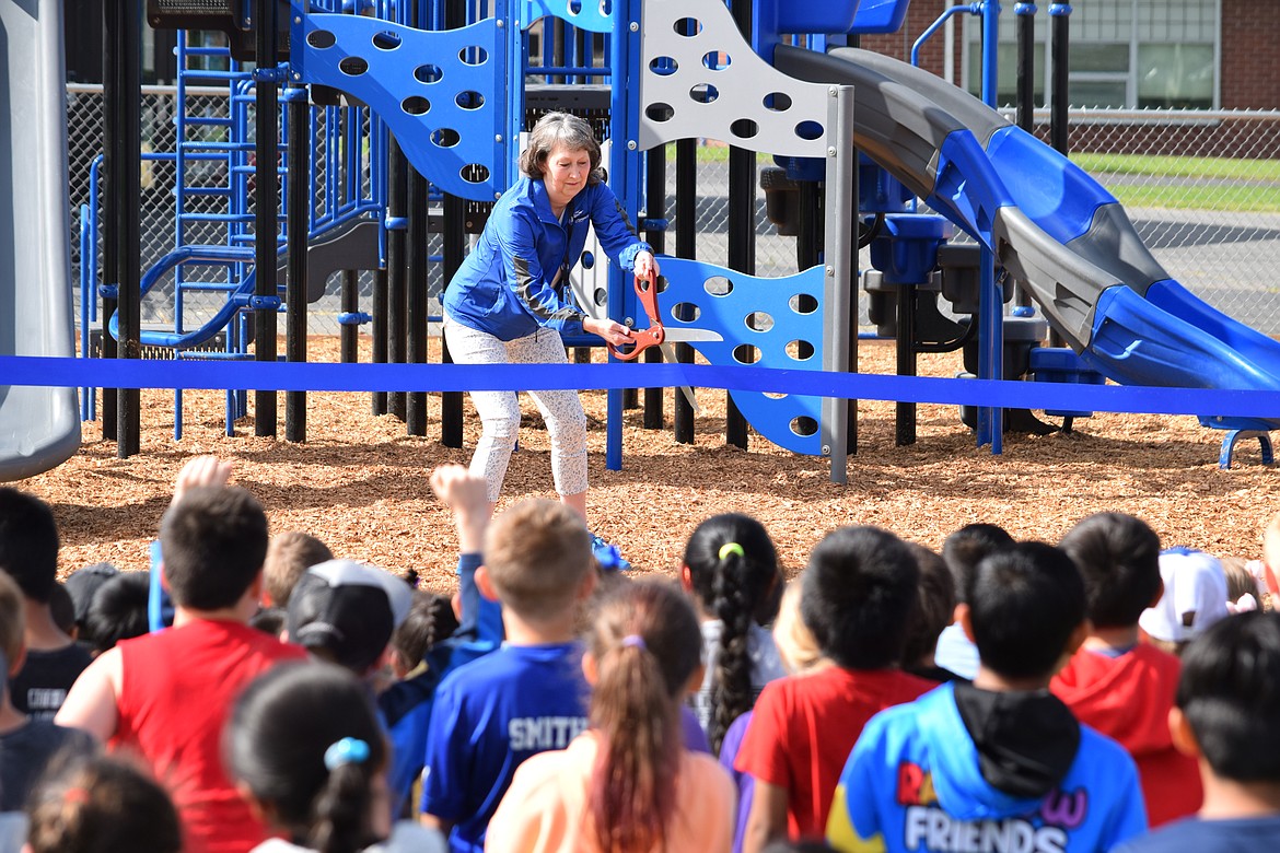 Jill Massa, director of teaching and learning for the Warden School District, prepares to cut the ribbon during a formal ceremony to celebrate the installation of two new sets of playground equipment at Warden Elementary School on Friday.