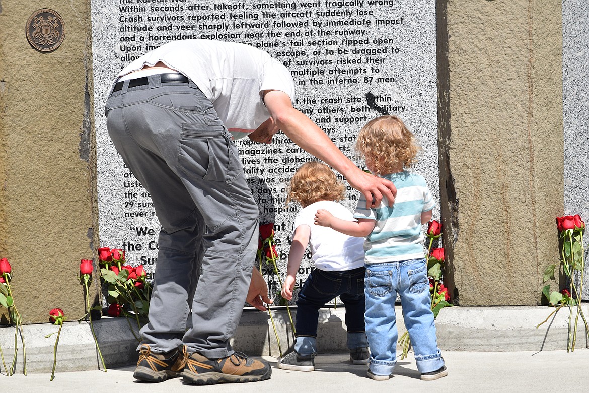 A man helps his two children lay roses at the 87 Forgotten Heroes memorial at the Port of Moses Lake on Monday.