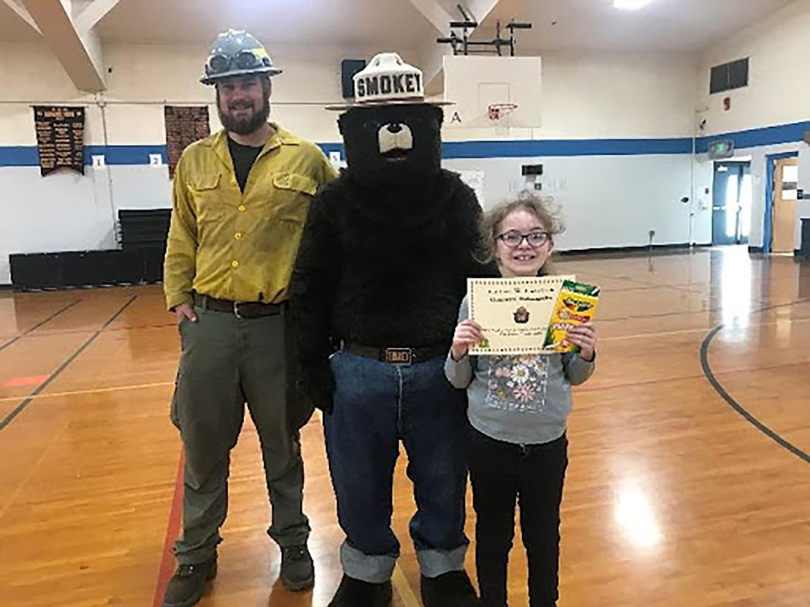 Priest River Elementary fourth-grade poster contest winner Charlotte McLaughlin pose with Smokey Bear along with Priest River Elementary graduate and U.S. Forest Service firefighter Conrad Ahlers.