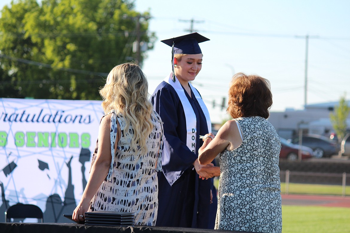 A Desert Oasis High School graduate receives her diploma with a solemn smile.