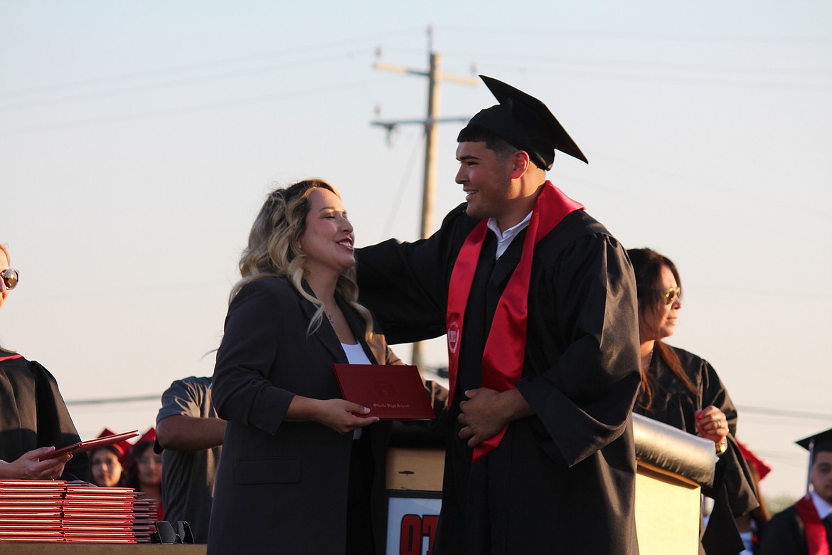 An Othello High School graduate gets his diploma and gives a hug from Othello School Board member Thalia Lemus.