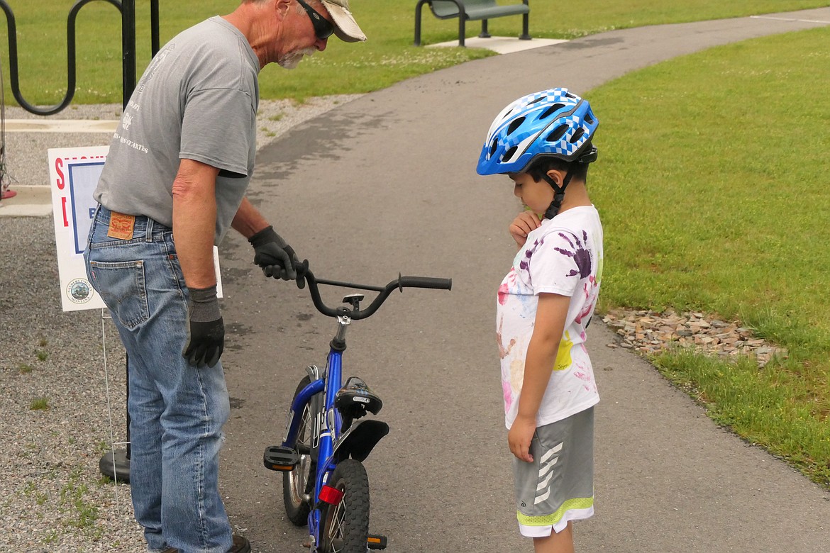 Thompson Falls repairman Tim Hoyt goes over mechanical safety check points with Kai Mosher, 7, of Thompson Falls as part of the Sanders County Public Heath bike safety event Saturday at Ainsworth Park. (Chuck Bandel/VP-MI)