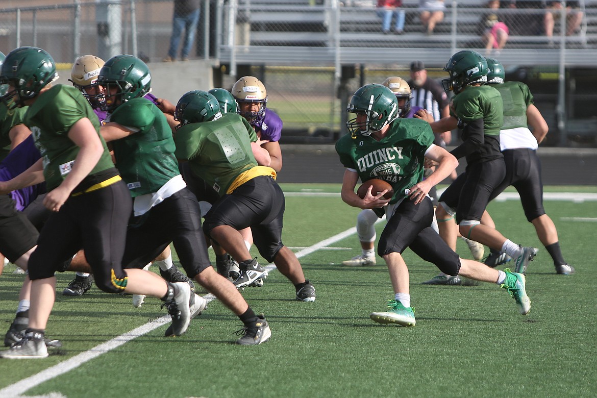 A Quincy running back runs behind a wall of offensive linemen against the Connell defense.