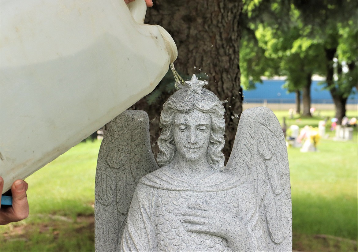 Water is poured on the statue of Michael the Archangel for cleaning on Wednesday at St. Thomas Catholic Cemetery.