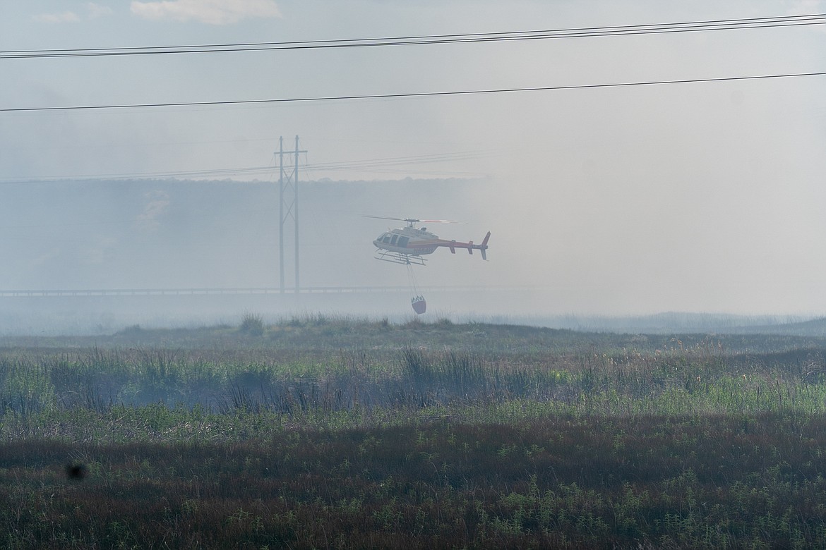 A helicopter flies through thick smoke to drop water on the fire near Rocky Ford Creek on Wednesday.