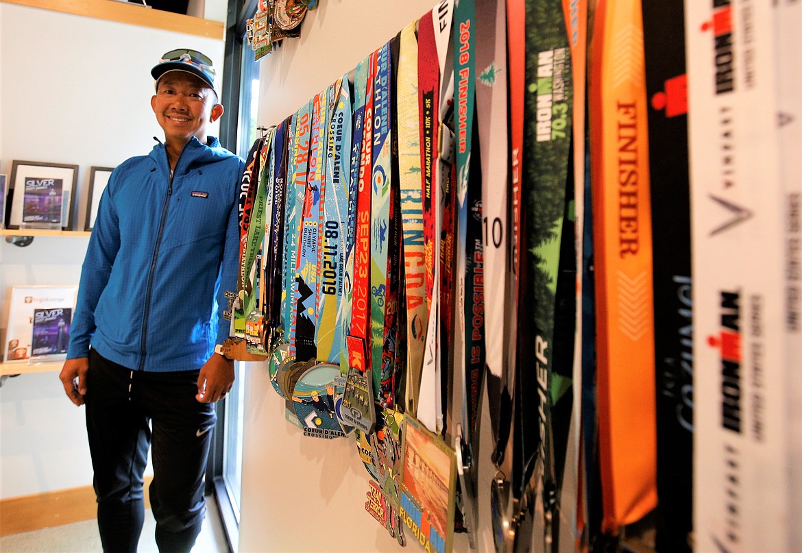 Ben Tran stands by medals he has earned for swimming, biking and running. The medals are displayed in the lobby of his Coeur d'Alene business.