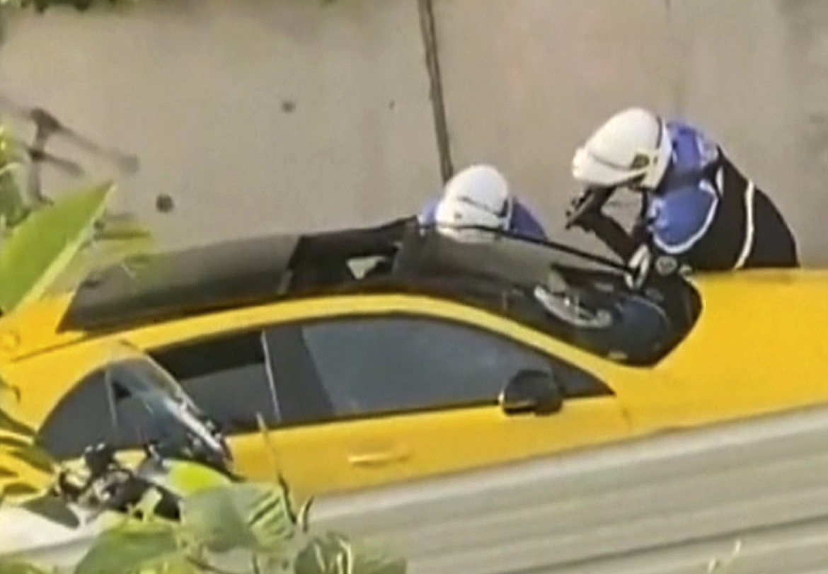 In this grab taken from video provided by @Ohana_FNG, two police officers question a driver, one pointing a gun towards the window of a yellow car, in Nanterre, France, Tuesday, June 27, 2023. France’s government has announced heightened police presence around Paris and other big cities and called for calm after scattered violence over the death of a 17-year-old delivery driver. The victim's lawyers say he was shot and killed Tuesday by police during a traffic check. Prosecutors say the police officer was detained on suspicion of manslaughter. (@Ohana_FNG via AP)