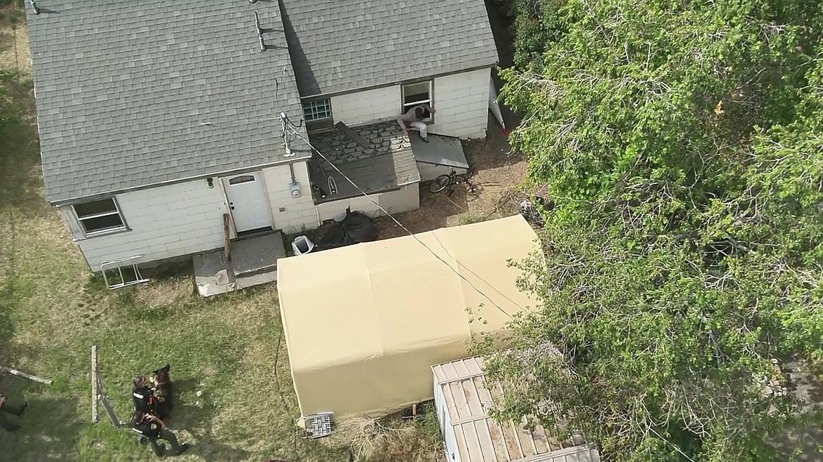 This image from a drone video shows Erik Milton of Soap Lake climbing out of a window in his residence to surrender to law enforcement officers, including K-9 Chewy.